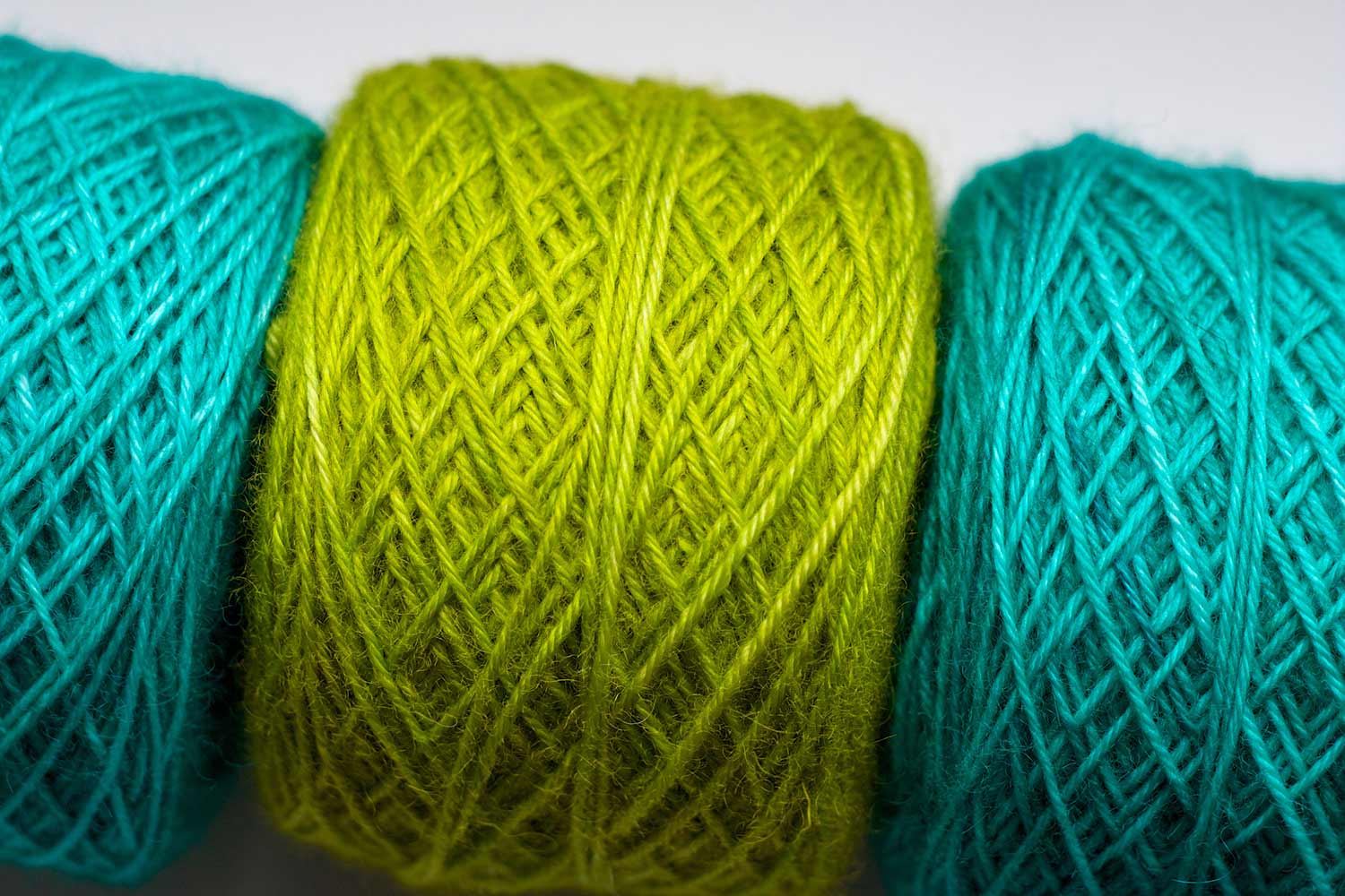Three yarn cakes lined up on their sides. Light teal, bright apple green, light teal.