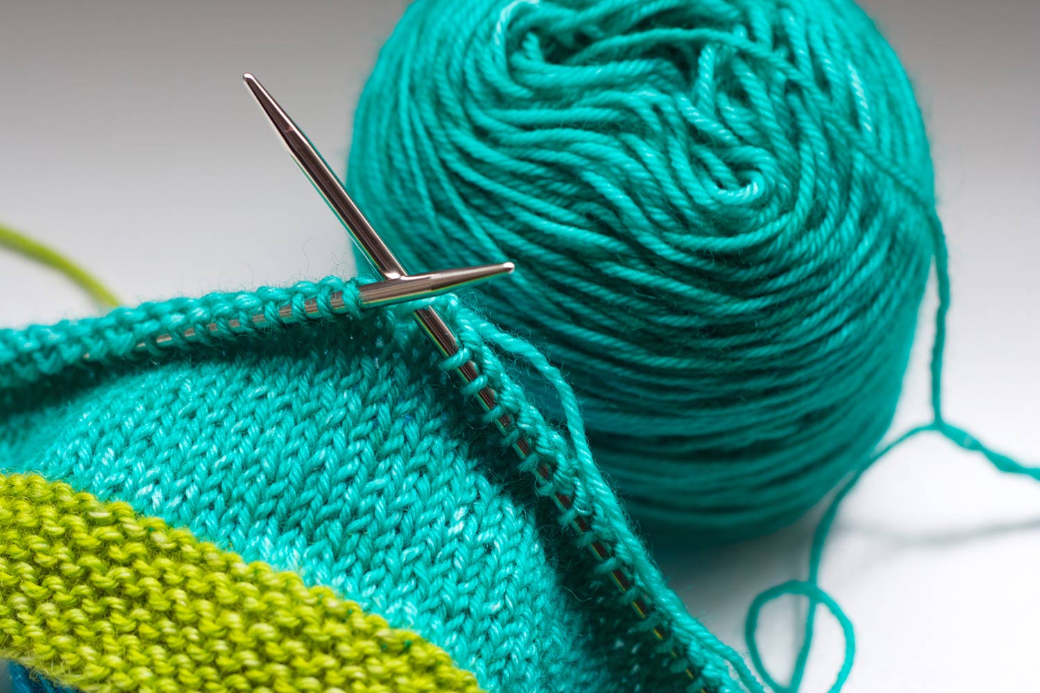 Light teal project with green trim on the needles next to ball of yarn.