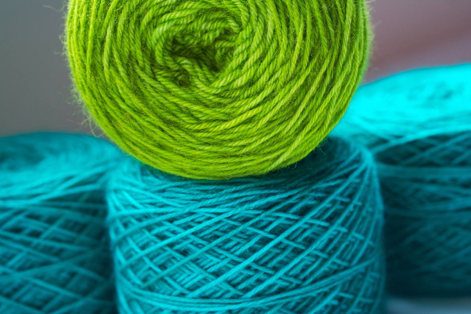 Light teal yarn cake with apple green cake stacked on top and several out of focus cakes in the background.
