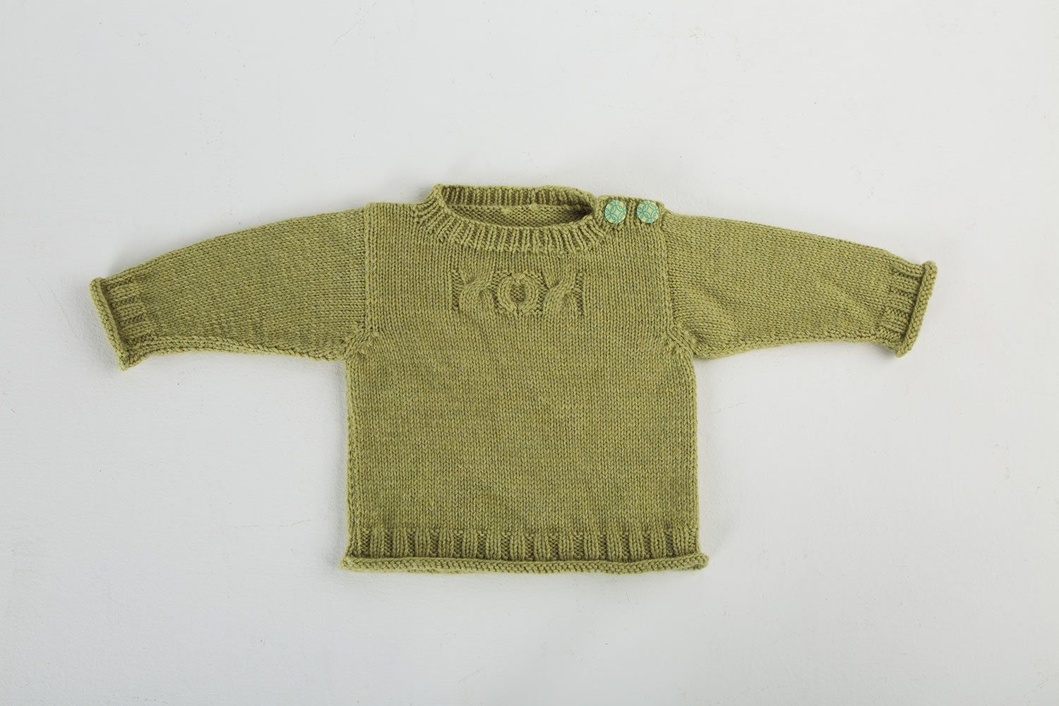 Baby sweater lying on white background with arms outstretched. Sweater is worked in stocking stitch with rolled hem and cuffs, plus ribbing at cuffs, hem and neck. Cables on chest read XOX.