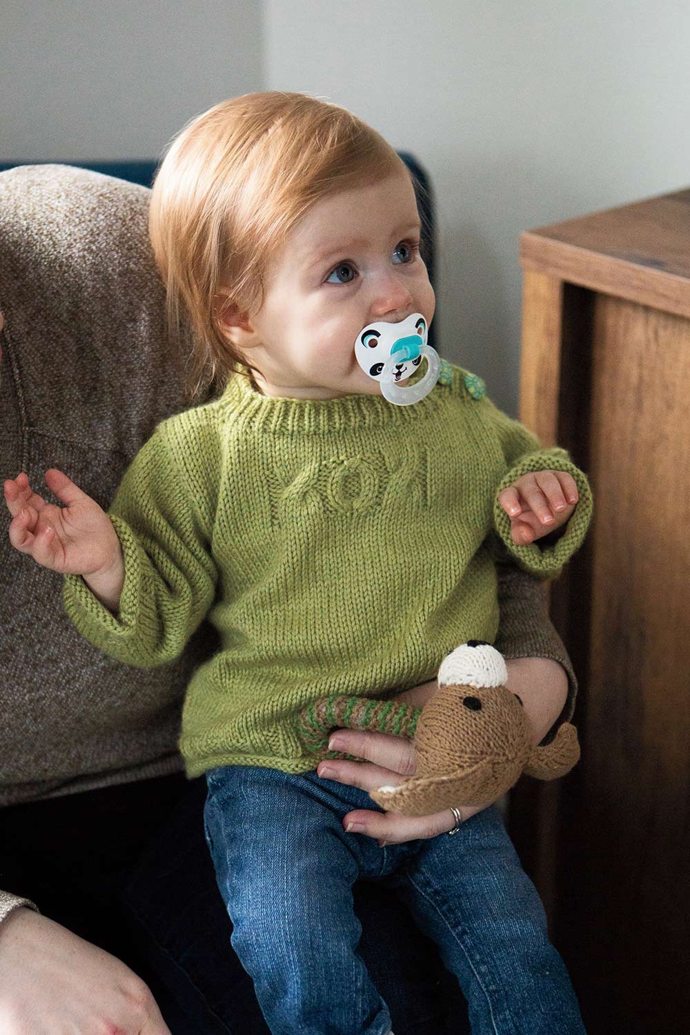 Baby on person's lap in oversized pullover with plenty of length pin the body and cute XOX created in cables on the chest.