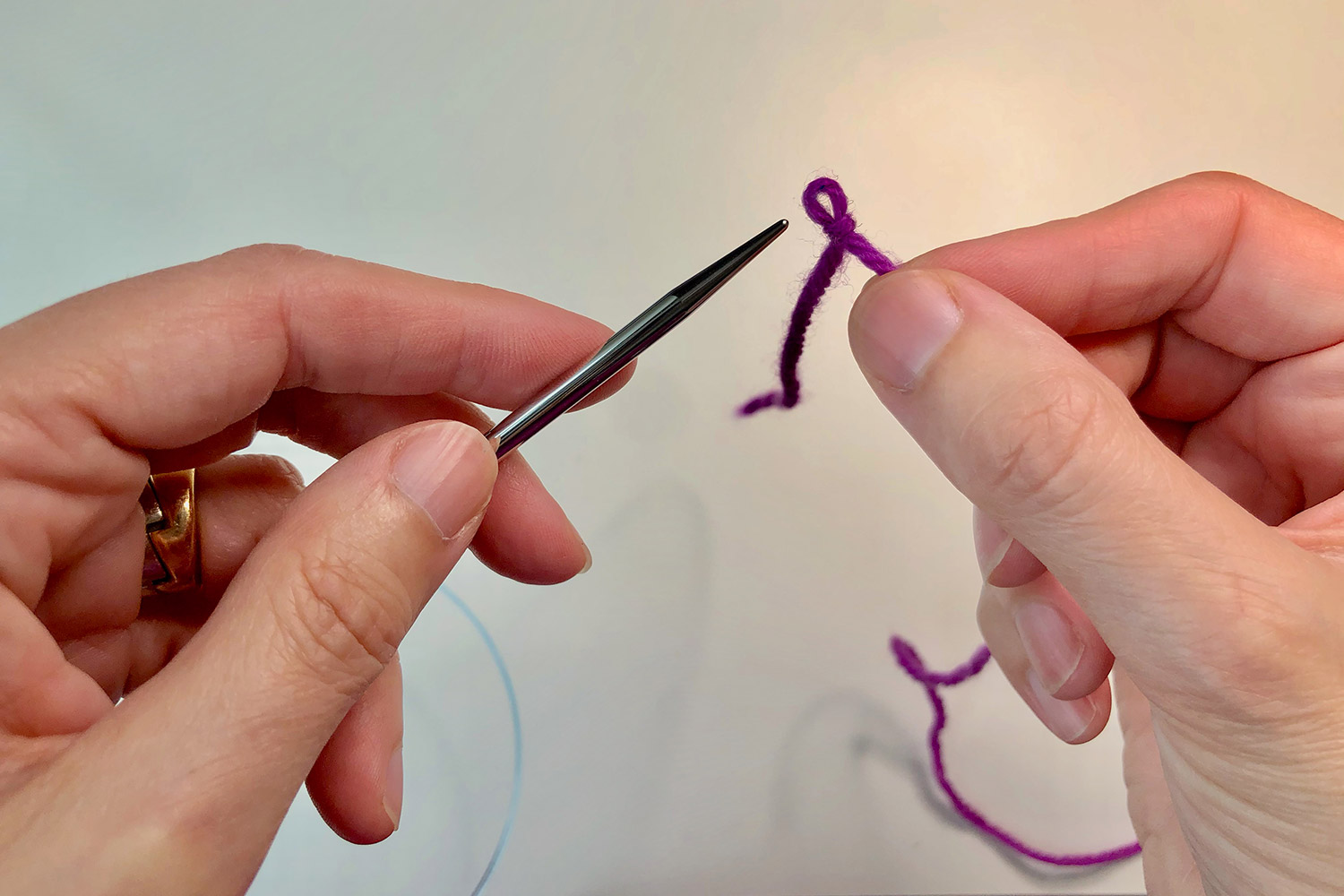 Hands directing a knitting needle into a slipknot.