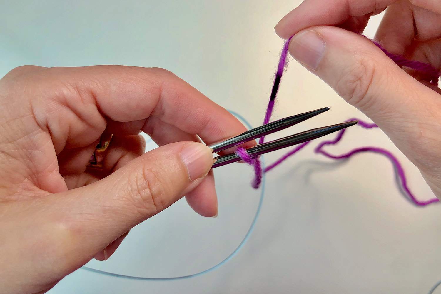 Hands holding two knitting needles together with a slipknot on the lower needle.