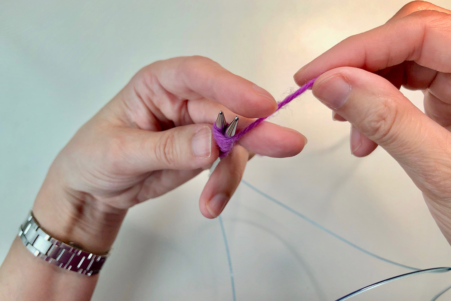 Two hands manipulating pink yarn that's wrapped around two knitting needles.