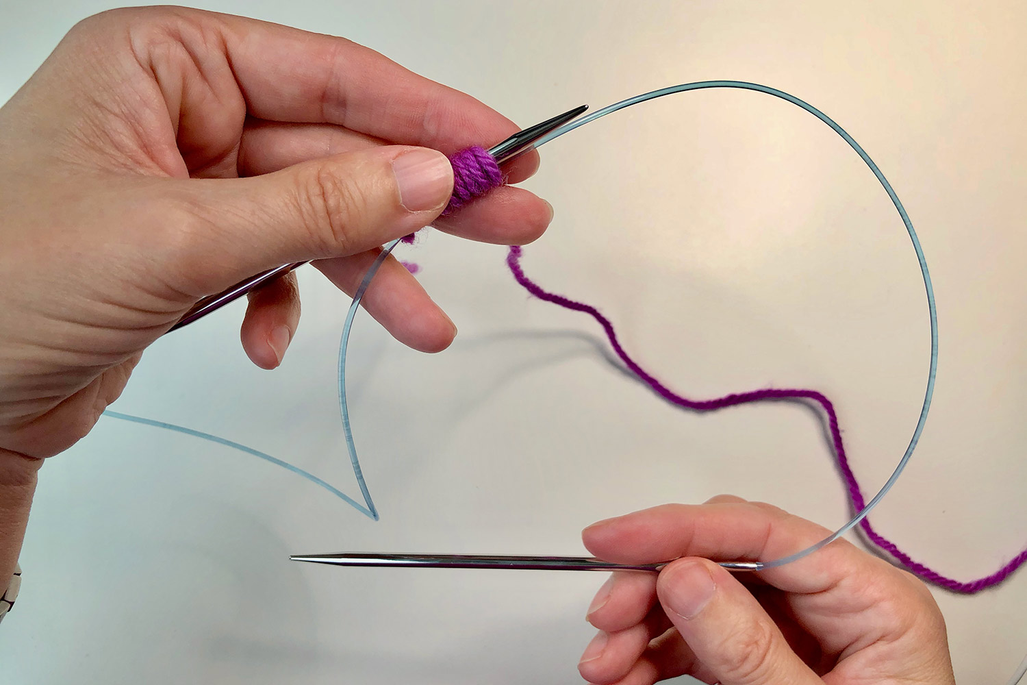 Yarn wrapped around two knitting needles with an arrow showing the direction to pull the lower needle.