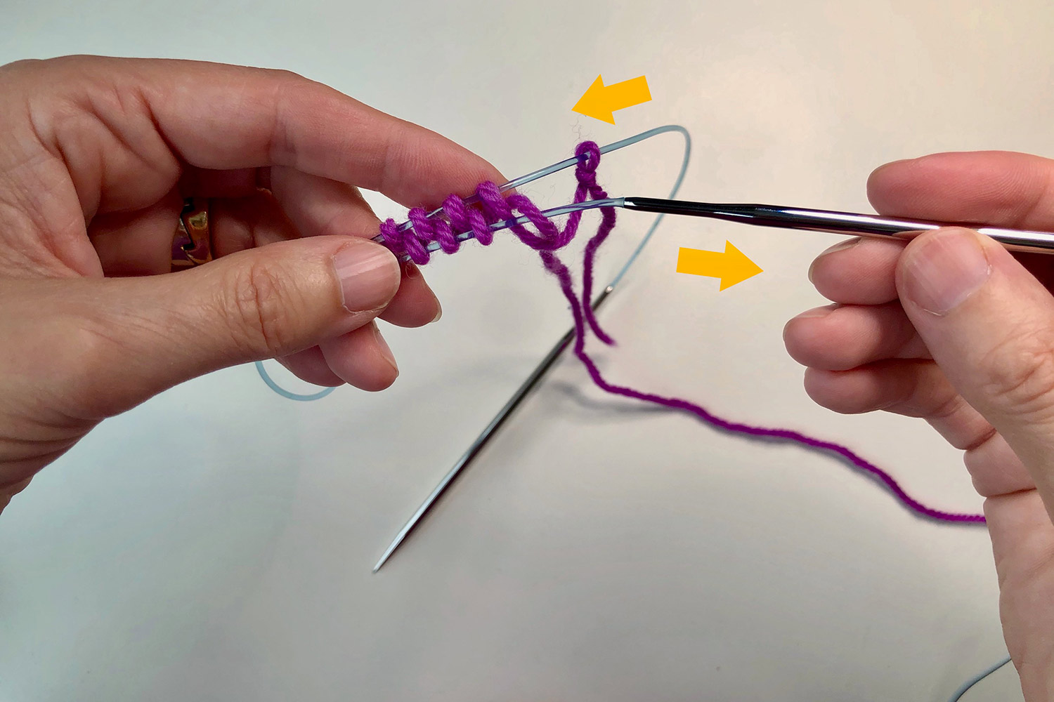 Loops of pink yarn around the cable of a circular needle and yellow arrows showing the direction to push/pull the needles.
