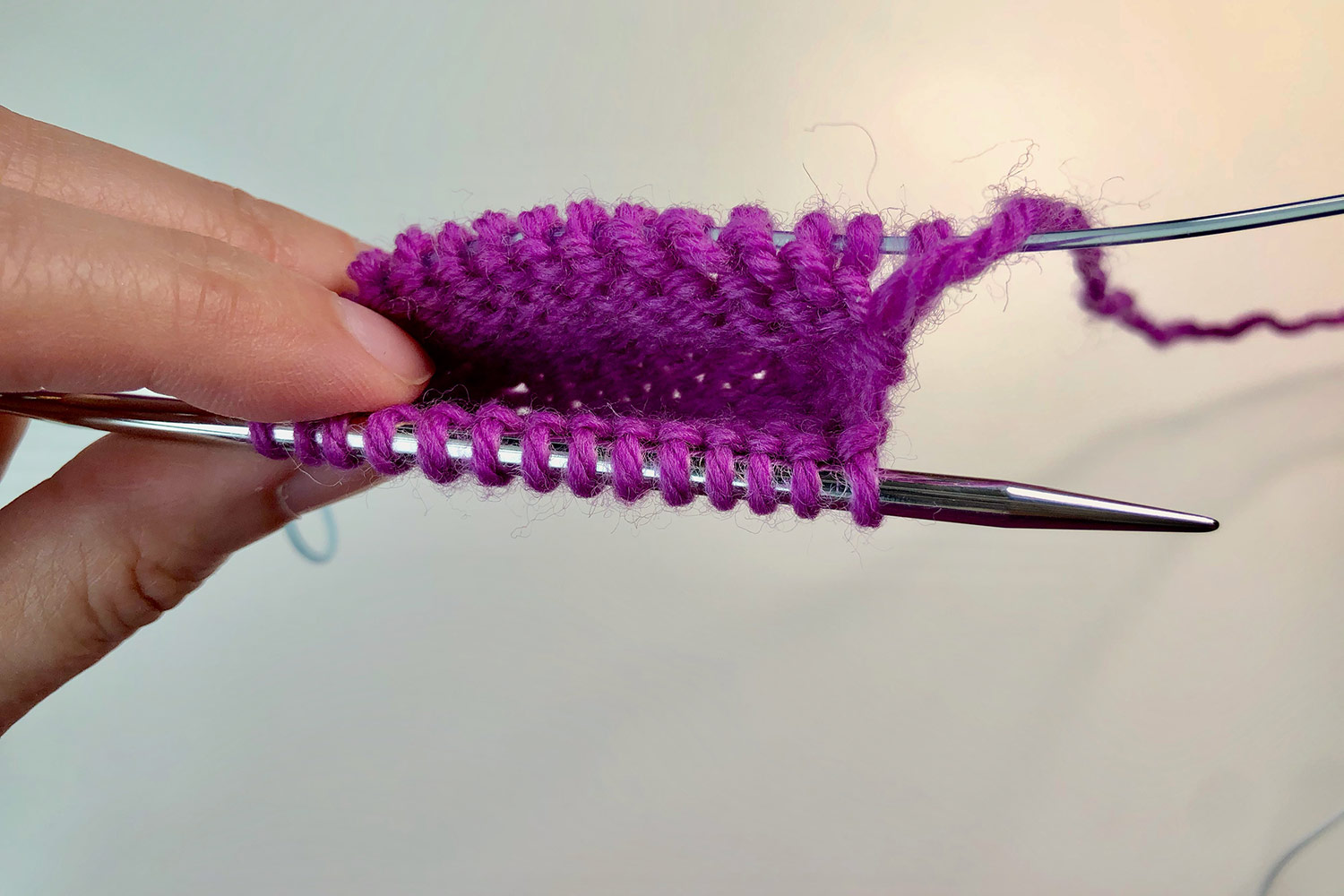 A hand holding the knitted toe of a sock, still on the a circular needle.