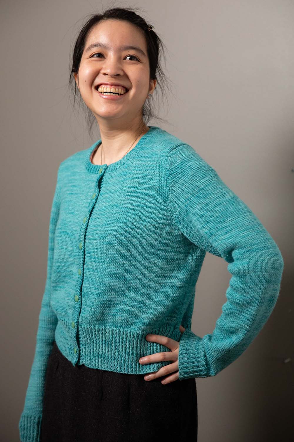 Woman with hand on hip wearing long-sleeved cardigan with round neckline.