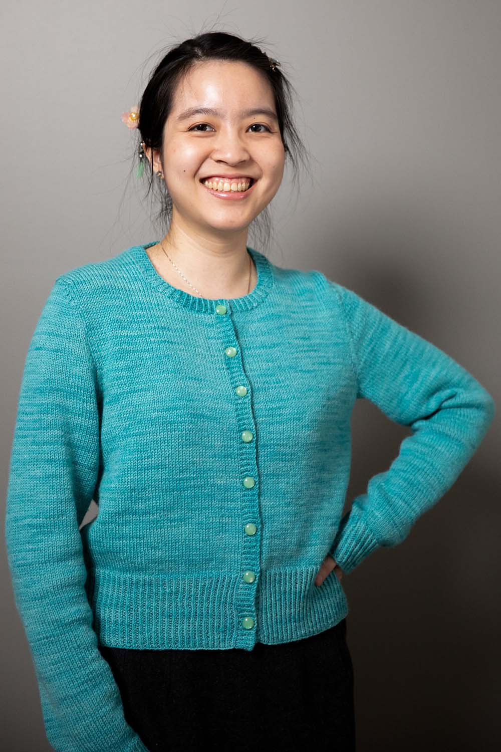Smiling woman wearing a round-neck cardigan in fingering-weight, turquoise hand-dyed yarn.