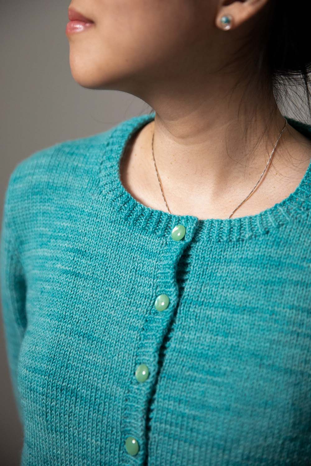 Detail shot of top four buttons and round neckline of modeled cardigan.