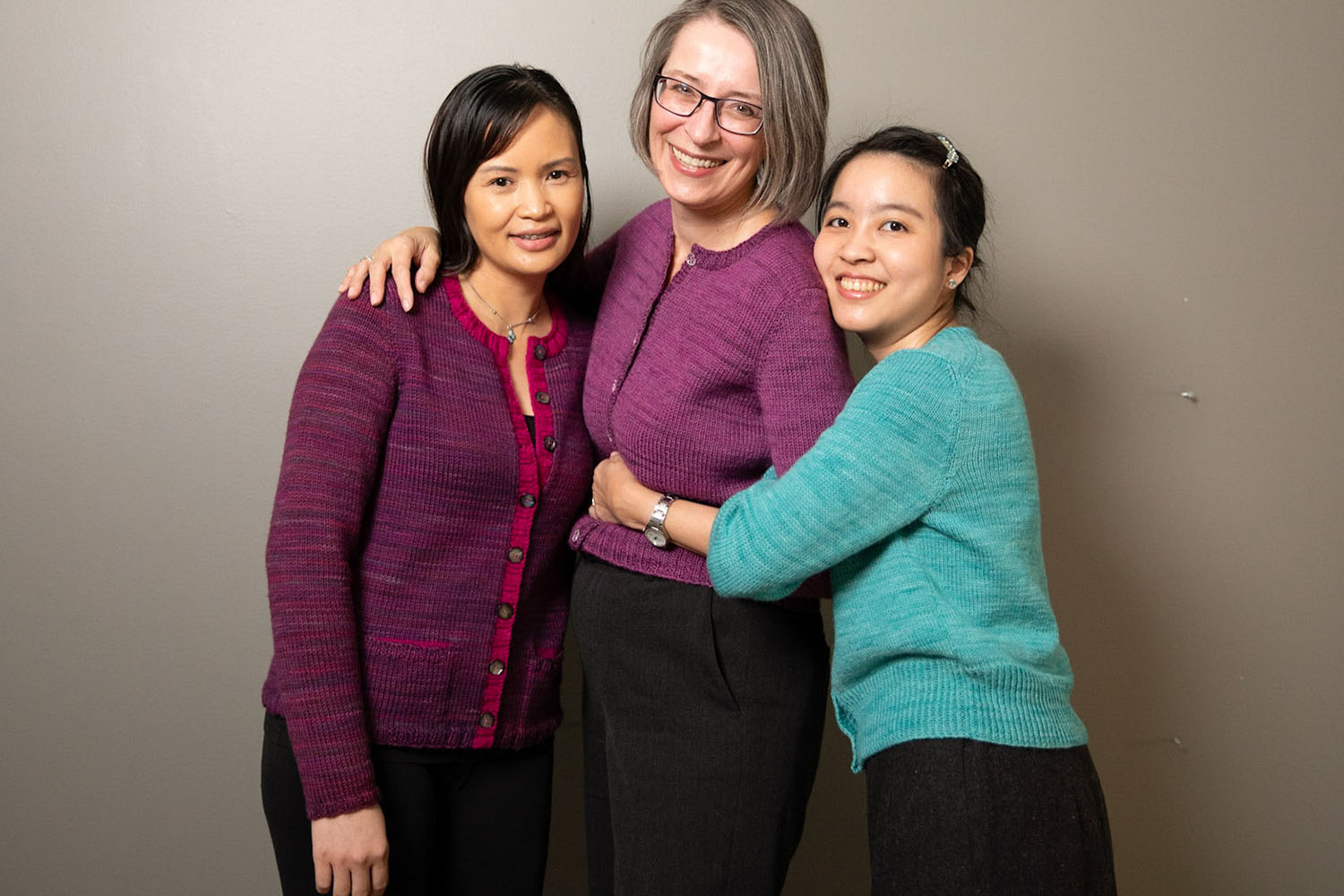 Three women wearing different variations of a round-necked cardigan in worsted weight, DK, and fingering weight yarn from left to right.