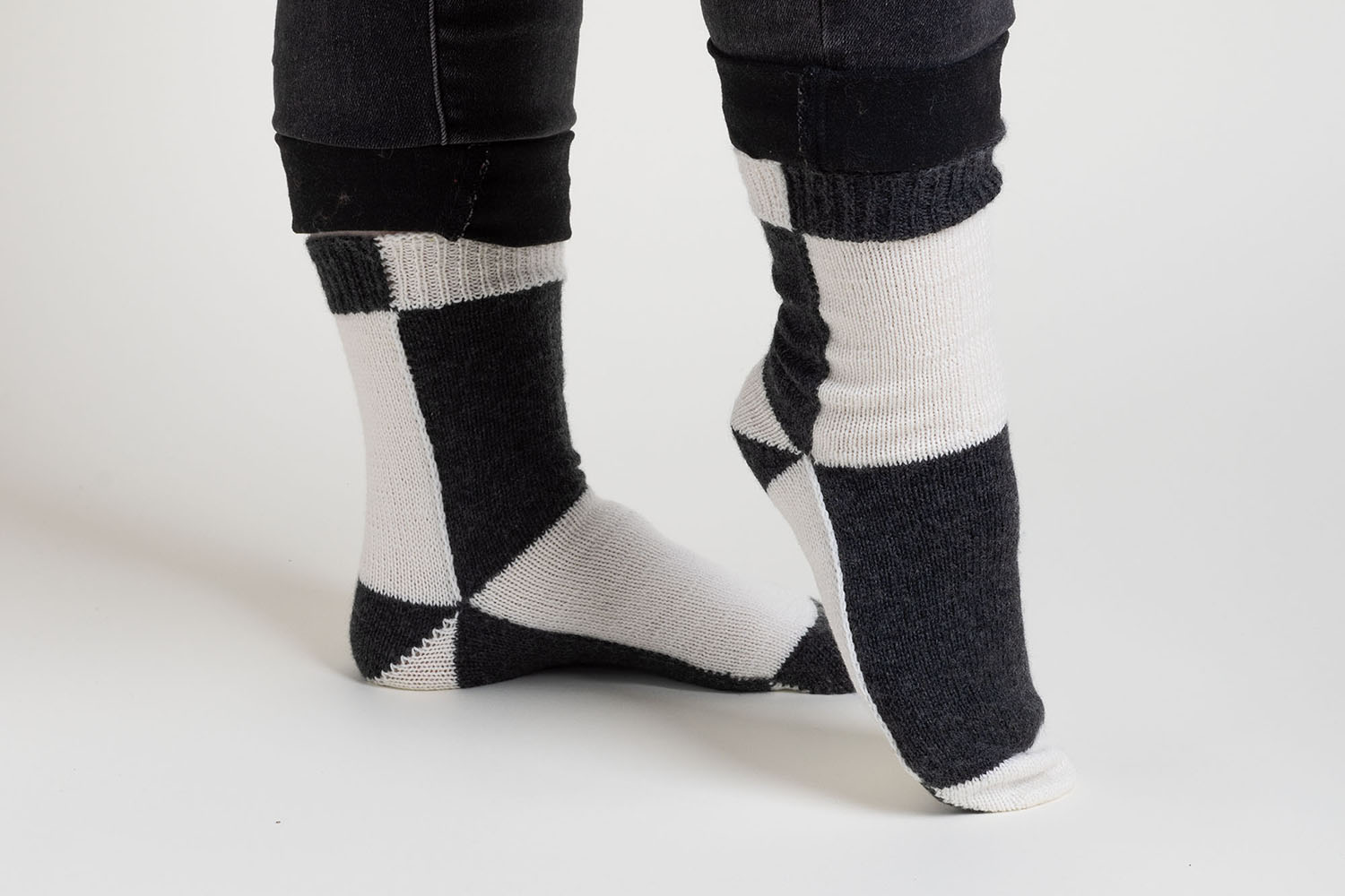 Side view of black and white colourblock socks worked flat; one foot is flat on floor, one foot is pointed.