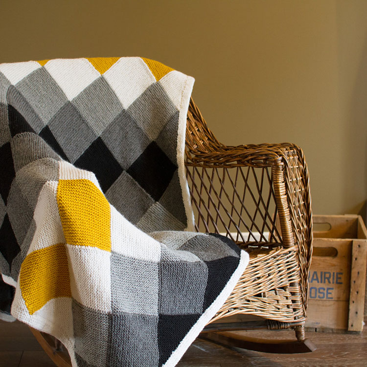 Entrelac blanket with stripes of diamonds in grey scale paired with a pop of colour, worked in squishy garter stitch with garter stitch border.
