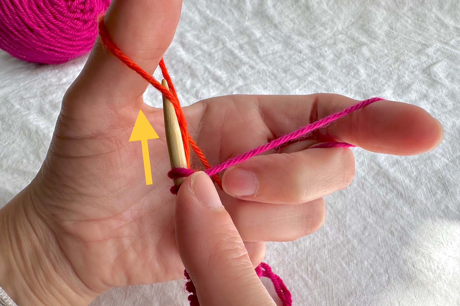 Needle inserted into thumb loop with directional arrow.