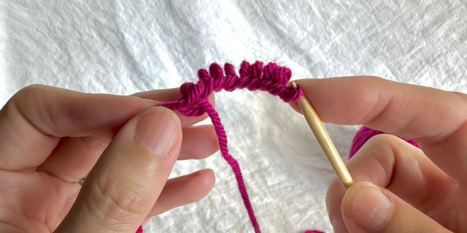 Ten cast-on stitches being slipped off needle while pinching tail at base of stitches and holding first stitch on needle.