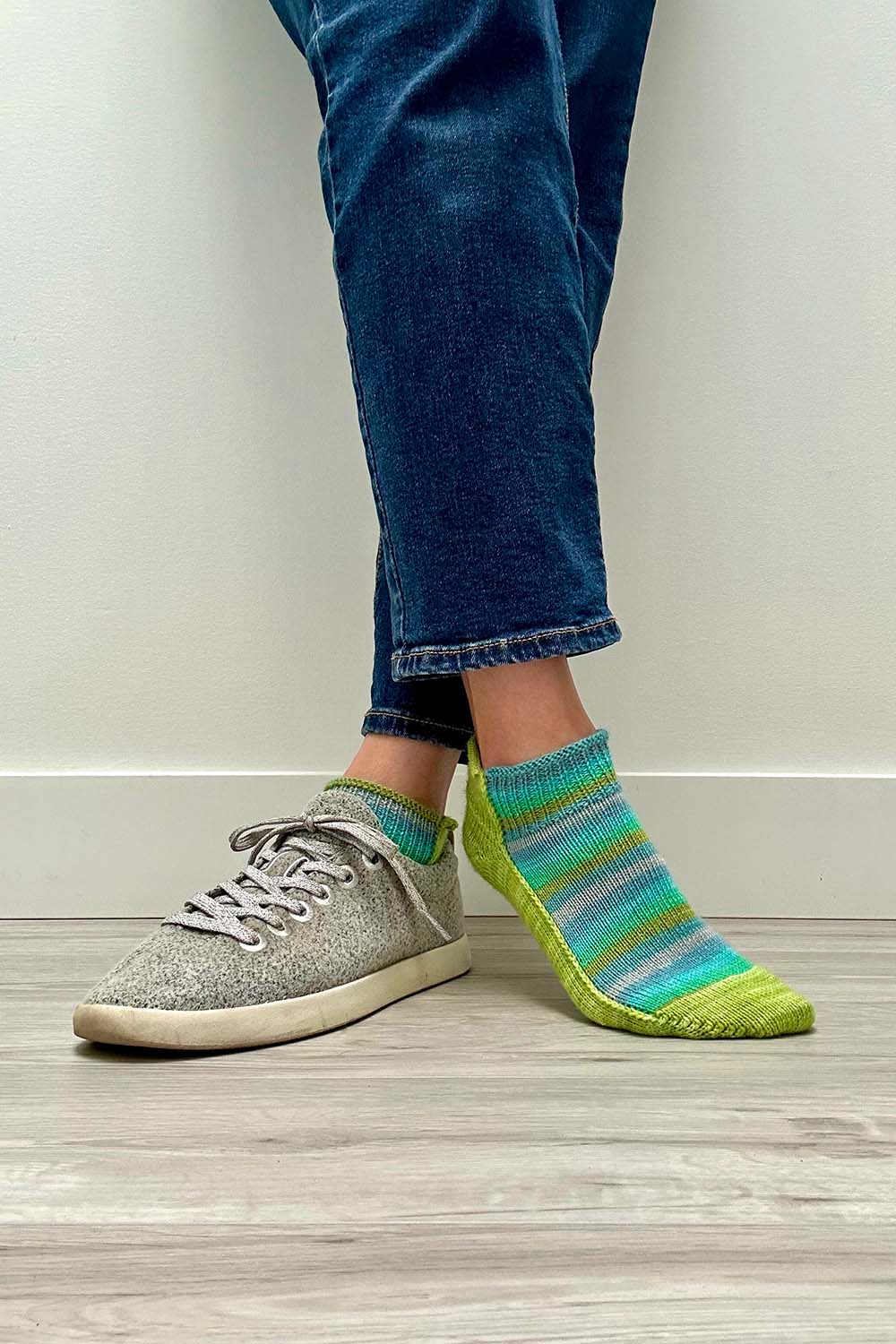 Front view of crossed legs, one shoe on and one shoe off while wearing shortie socks.