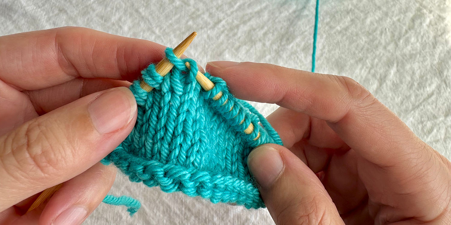 First step of a right raised increase; the right needle is inserted into right side of stitch in row below next stitch on needle.