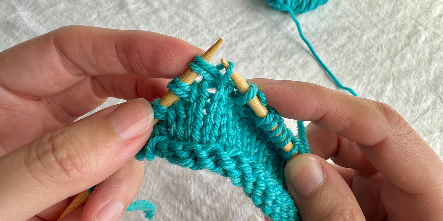 With right side facing, right needle is inserted into stitch in row below the twin stitch on left needle.