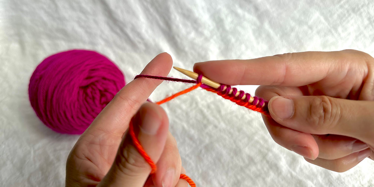 Two hands working long tail cast on and forefinger of right hand is holding a space on needle between last two stitches worked.