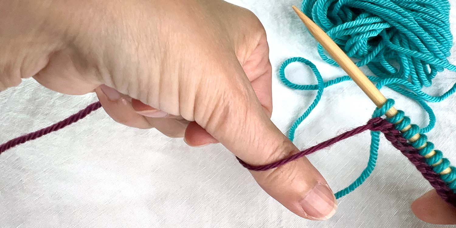 Newly cast on stitches on needle held in right hand while left hand points thumb down behind tail strand of yarn held in hand.