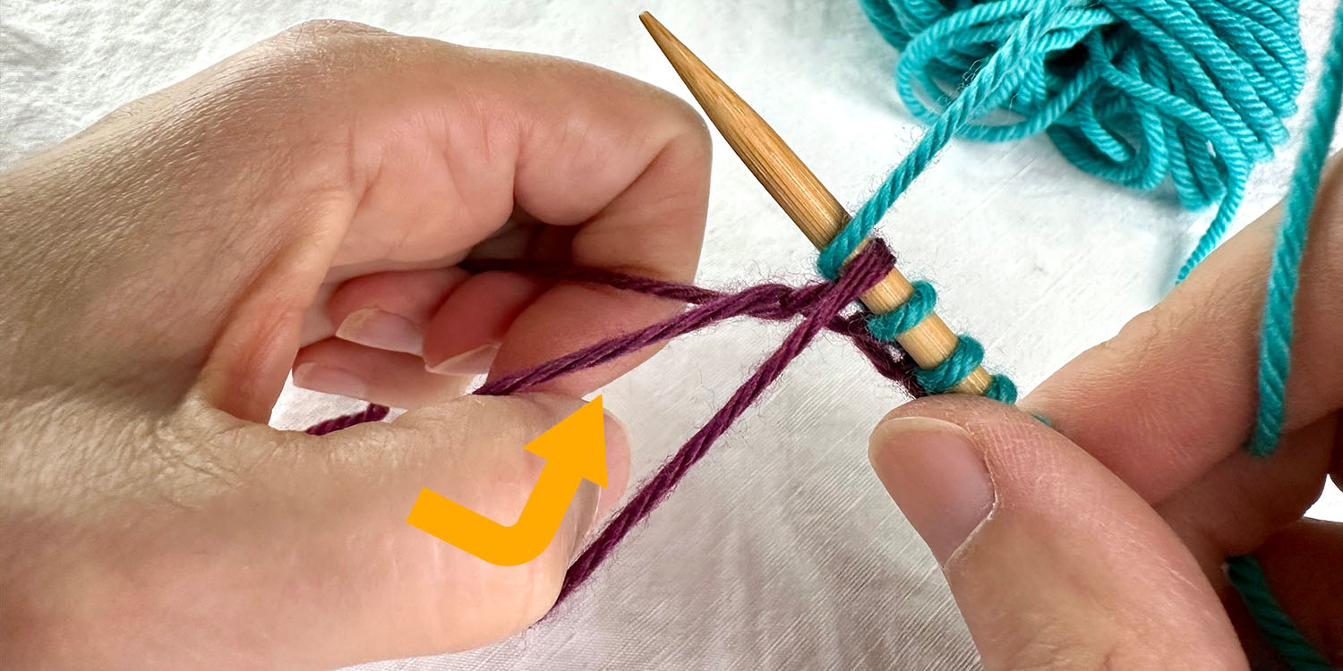 Needle in right hand and left hand holding tail yarn and a loop around thumb. Thumb has been bent inwards which has untwisted the loop around thumb.
