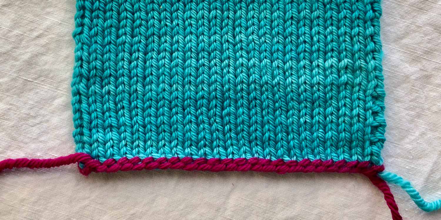 Stocking stitch swatch with the tail of the Old Norwegian Cast On shown in pink. It looks like a typical long tail cast on with purl bumps above.