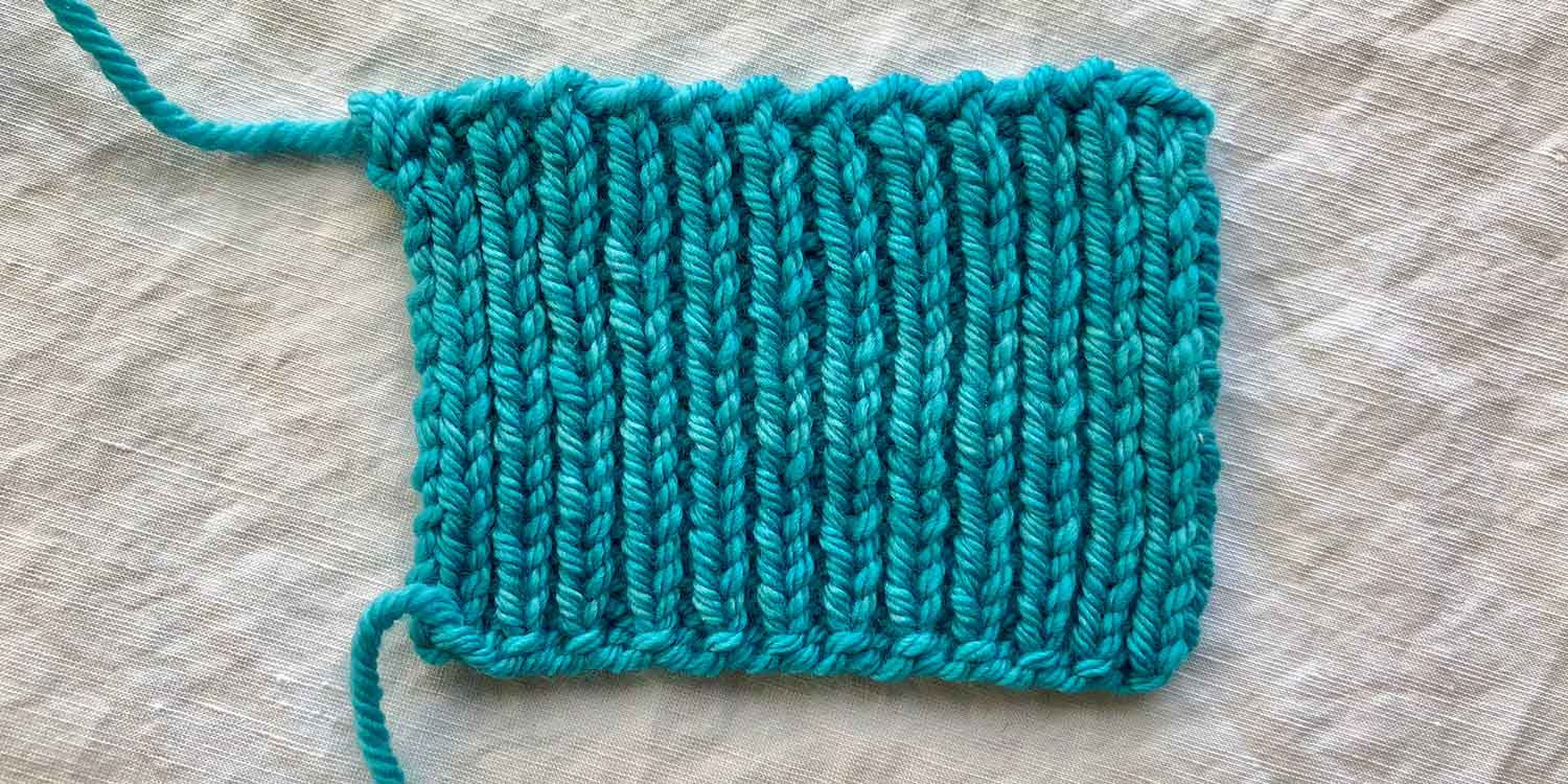 Swatch of ribbing with an Old Norwegian Cast on along lower edge. The base of each knit column of stitch looks like it has a little purl bump just after the cast on edge.