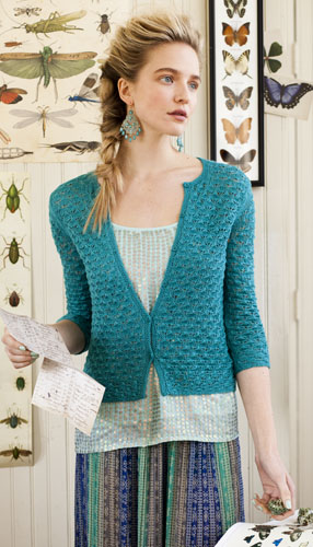 Magazine shot of model wearing turquoise lace cardigan; her body faces the camera and she's looking to the side.