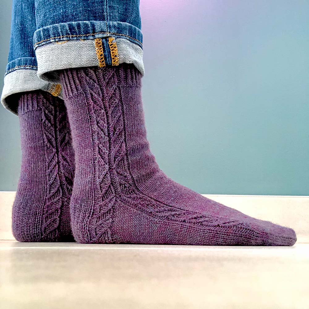 Top down socks with twisted stitch detailing running down side of leg and splitting to round down side of foot and side of heel.