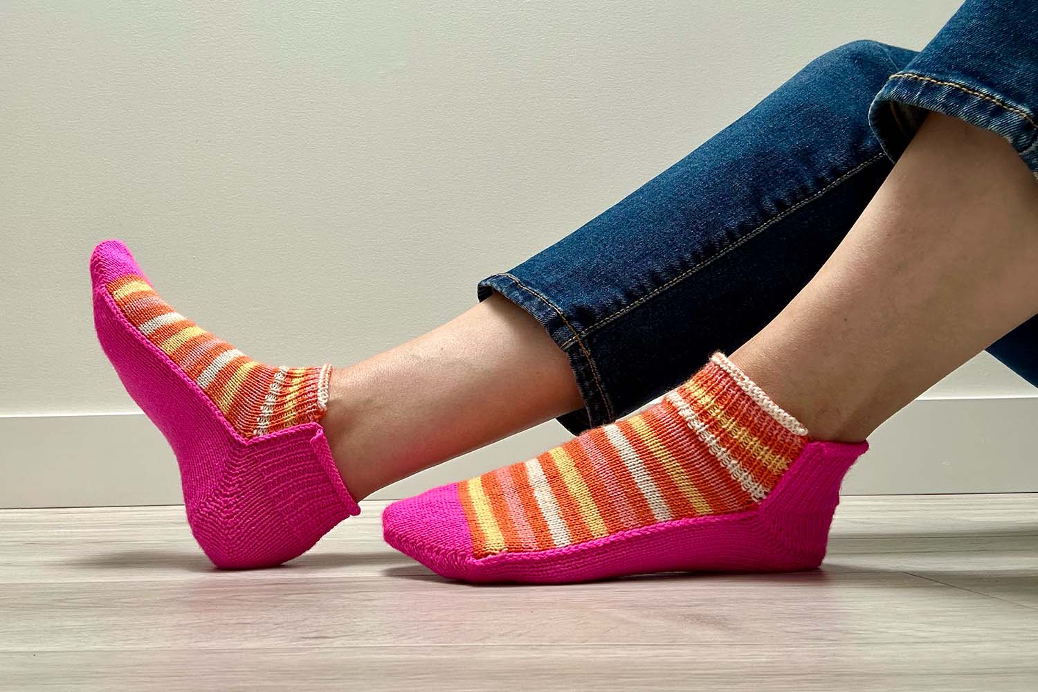 Profile view of shortie socks while sittign on the floor, showing solid-coloured sole and striped instep.