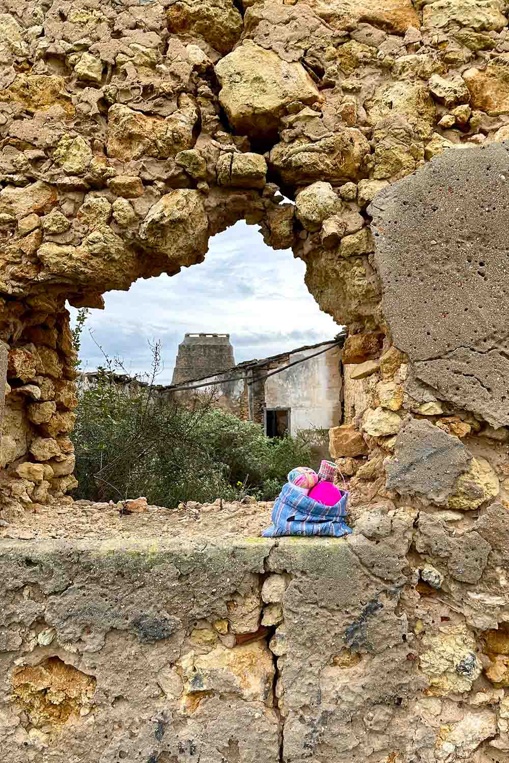Knitting project bag sitting on the window will of a stone constructed building in ruins.