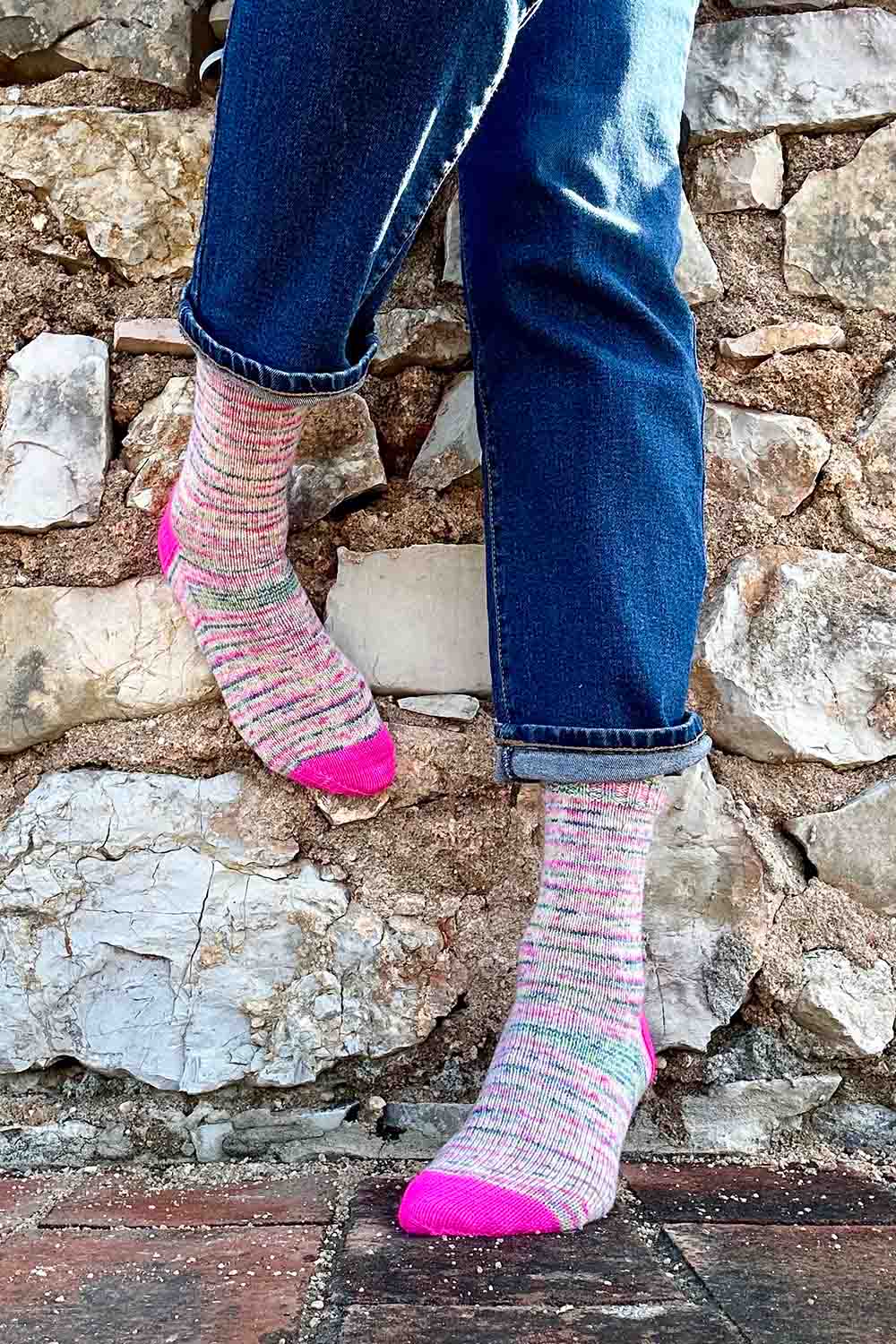 Speckled socks with hot pink toes and heels modeled in front of rock wall.