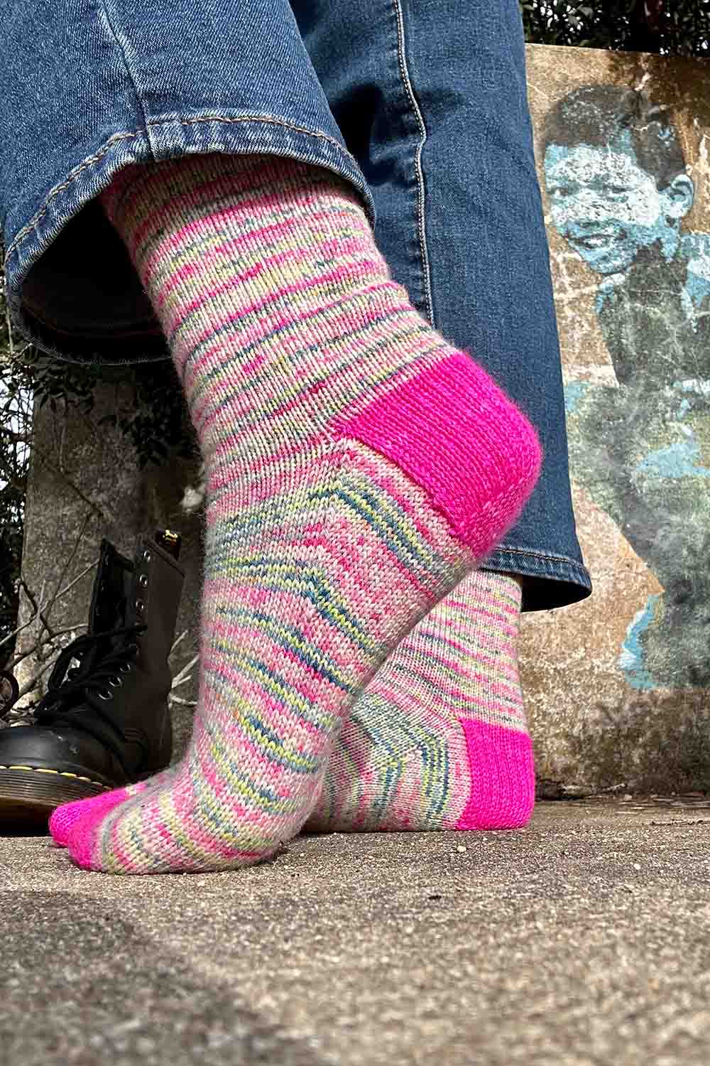 Side view of handknit socks with deep heel flap standing in front of wall with graffiti art.
