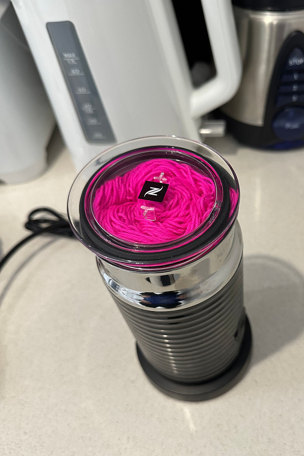 Nescafe milk frother with transparent lid on and a bright pink ball of yarn in receptical.