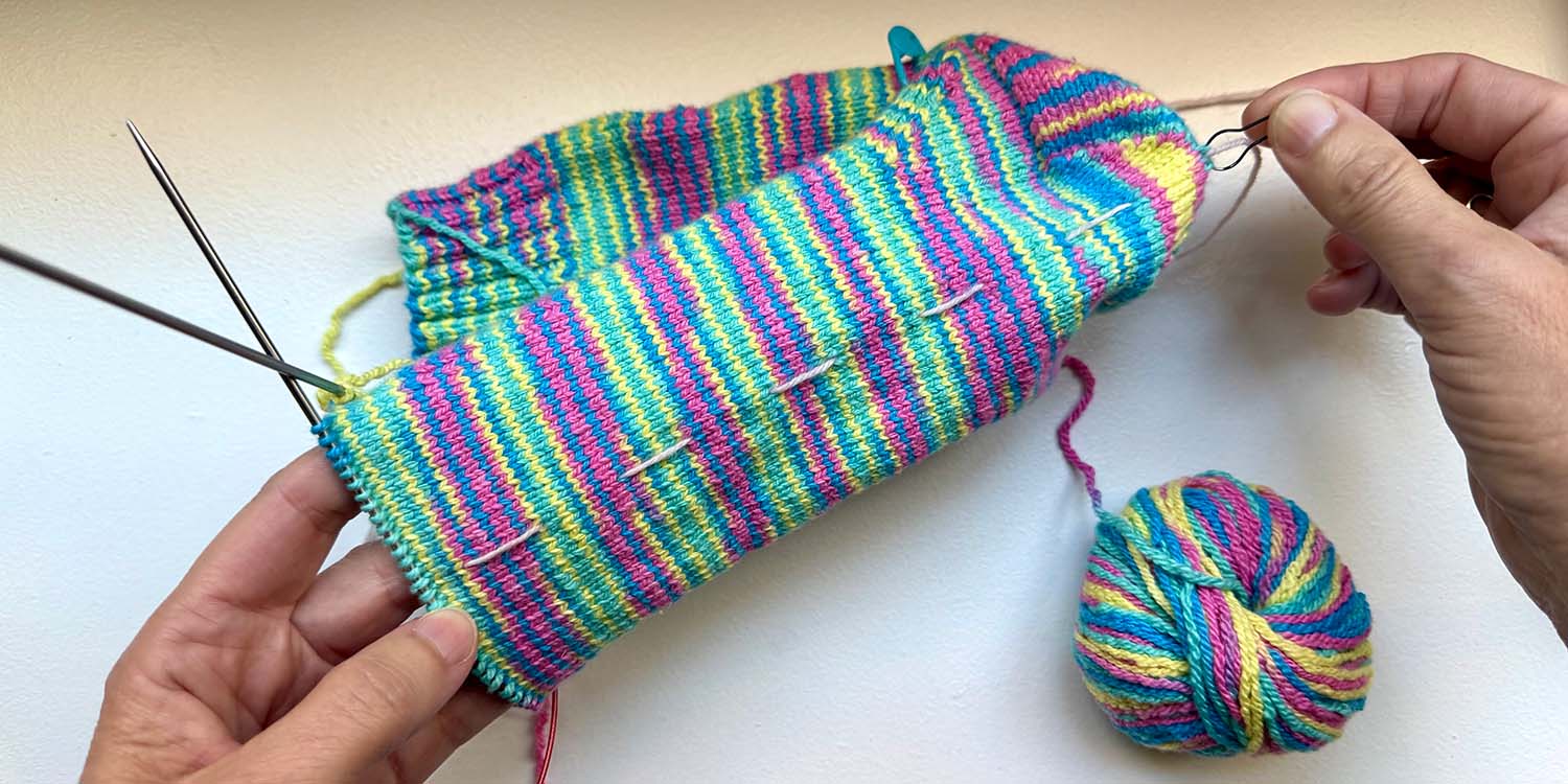 Sole of sock in progress with yarn marker used for counting rounds and stitch marker at base of heel used for measuring foot length.