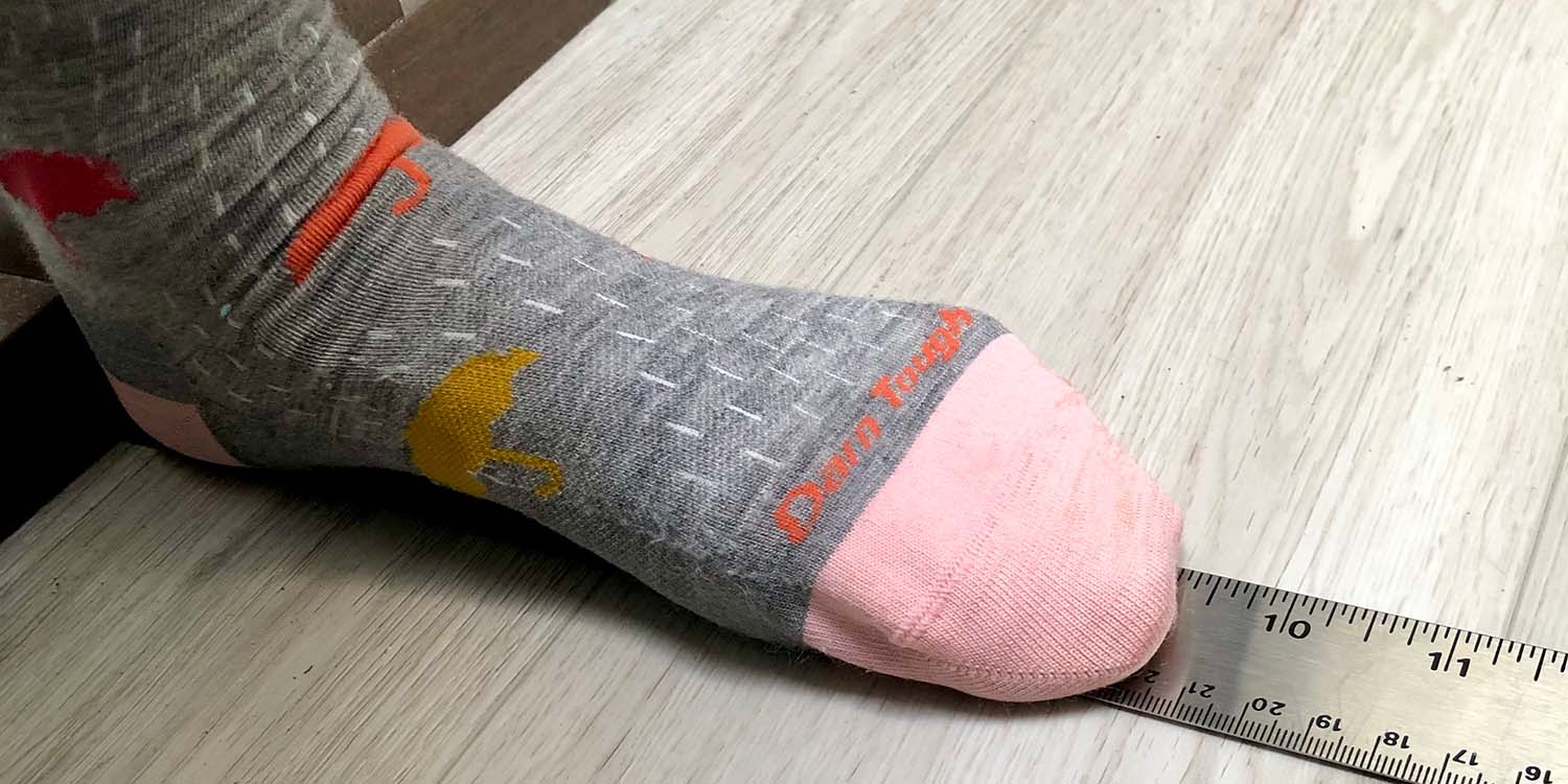 Stocking foot standing against a wall and standing on a ruler; the foot is 9 1/2" long.